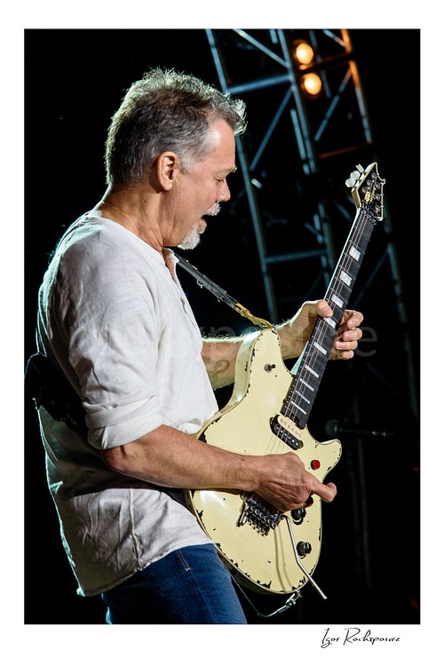 Vertical color image of Eddie Van Halen of Van Halen performing live with a white electric guitar in a close-up stage portrait
