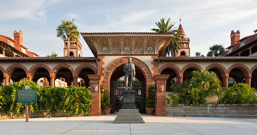 Henry Flagler statue standing before the historic entrance archway of Ponce de Leon Hall in St. Augustine.