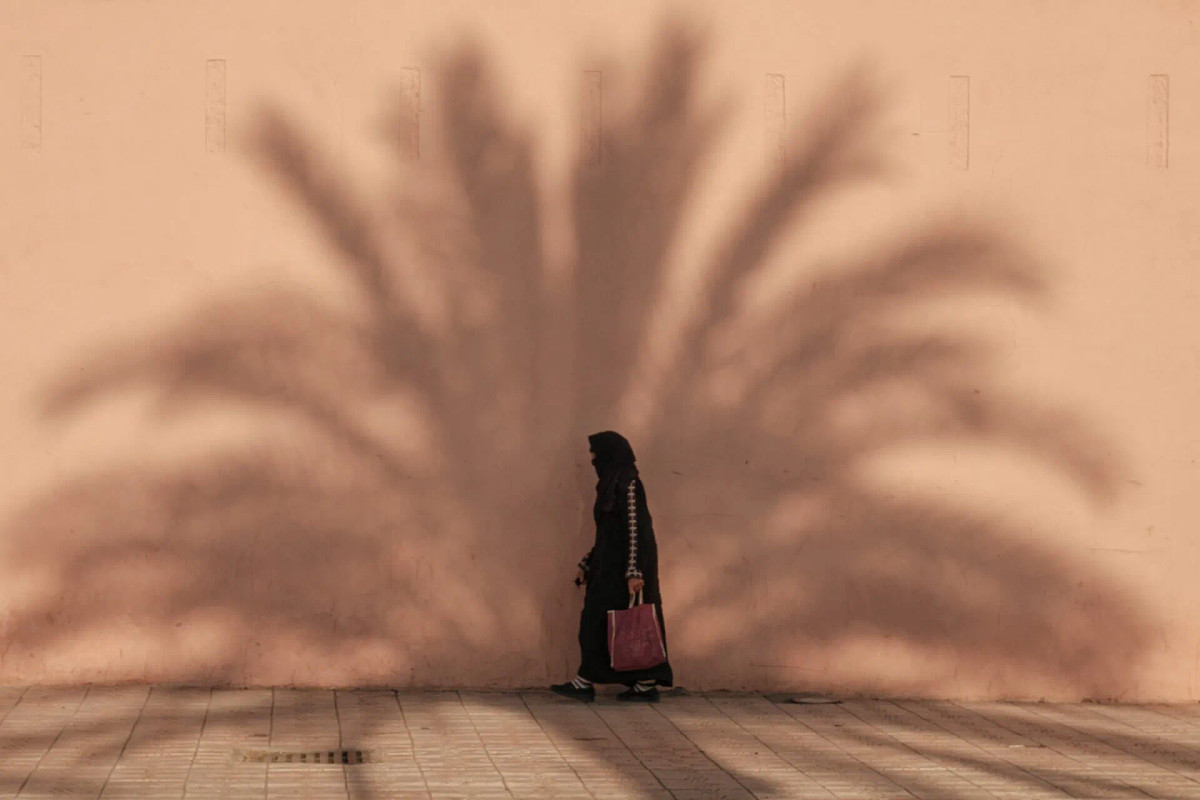 A woman in the shade of a palm tree at the pink walls of Marrakech