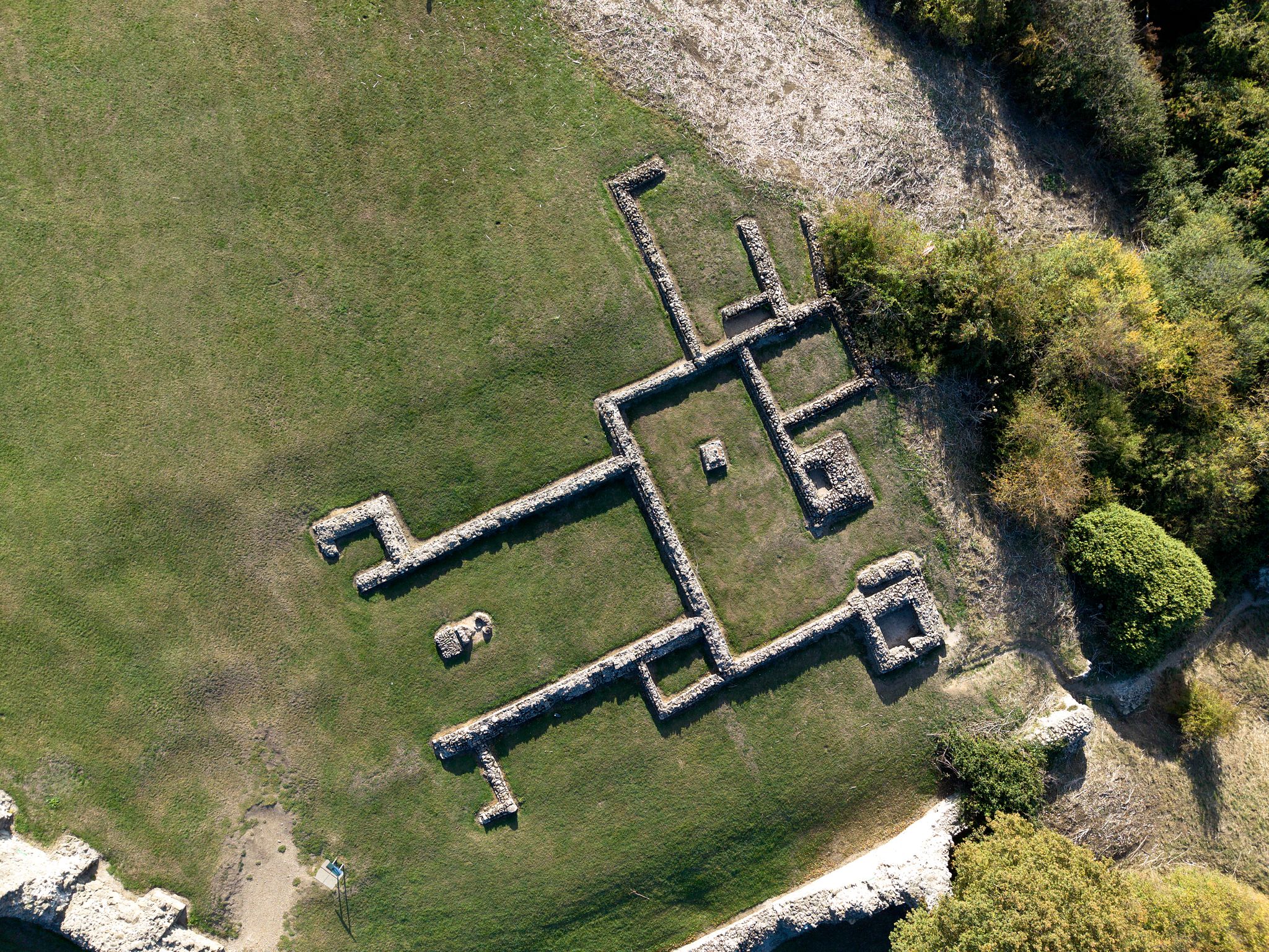Aerial drone photograph of historic stone foundations surrounded by grass and woodland, viewd from directly above.