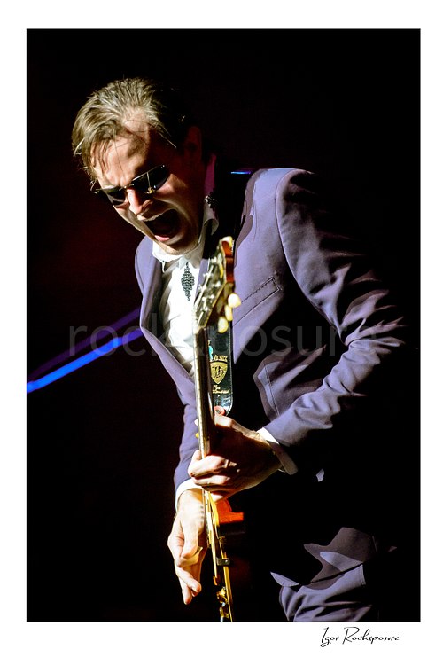 Vertical color image of Joe Bonamassa performing live on stage with a guitar in a dramatic close concert portrait