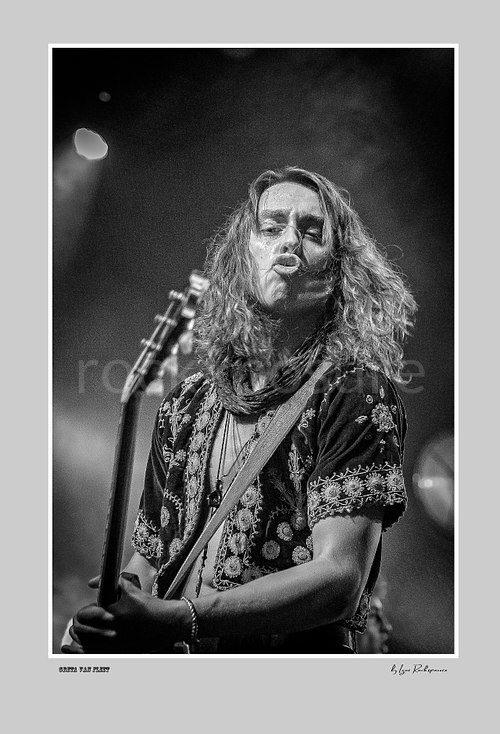Vertical black and white image of Greta Van Fleet bassist Sam Kiszka performing live on stage