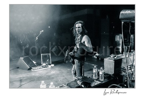 Horizontal black and white image of Nuno Bettencourt standing on stage with his guitar and giving a thumbs-up toward the camera