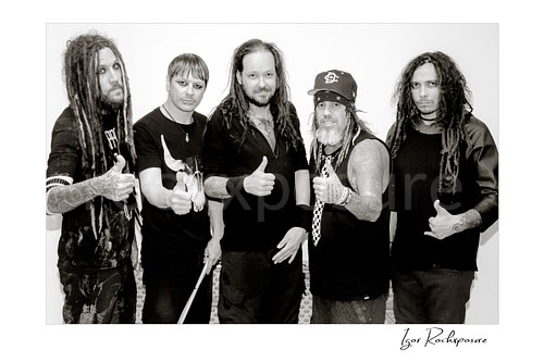 Horizontal black and white image of Korn members posing together in a backstage hallway portrait
