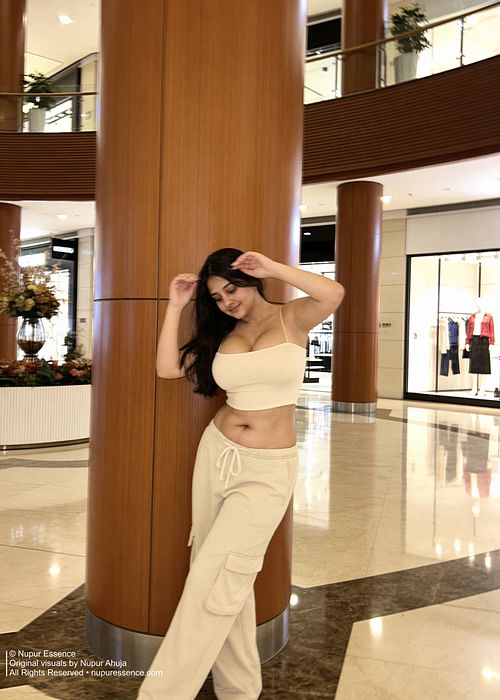 Nupur Ahuja posing beside a wooden architectural column wearing a beige fashion outfit in a shopping mall, published by Nupur Essence