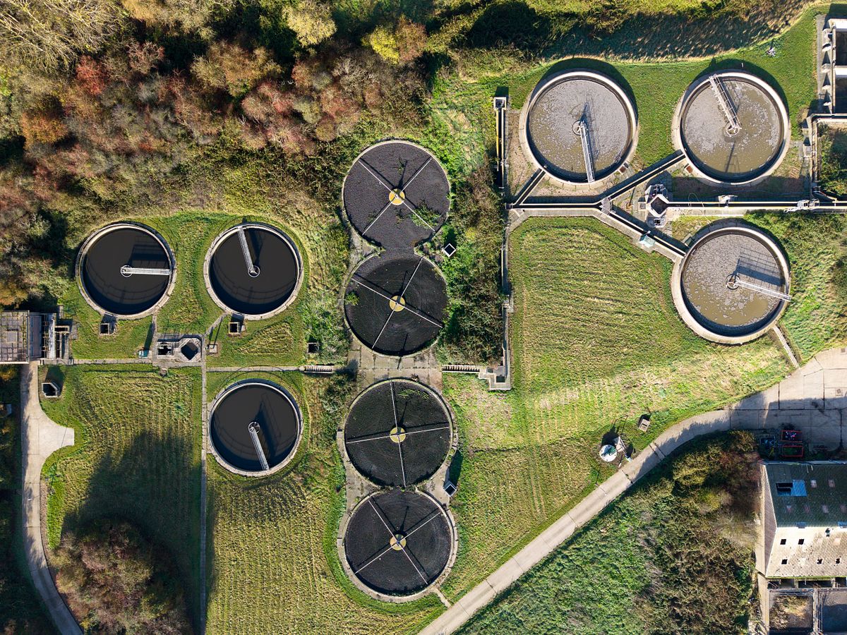 Aerial drone photograph of circular industrial tanks surrounded by woodland and patterned landscape.