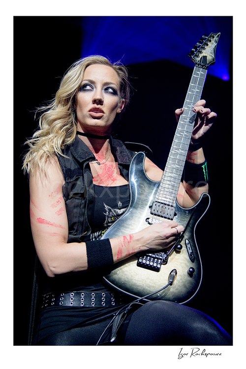 Vertical color image of Nita Strauss performing live on stage with an electric guitar in a close concert portrait
