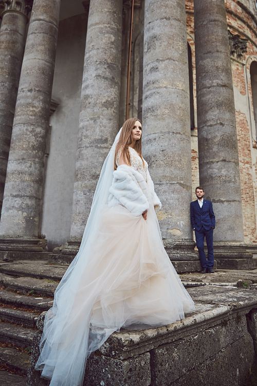 Bride and groom beneath the historic church columns in Pidhirtsi