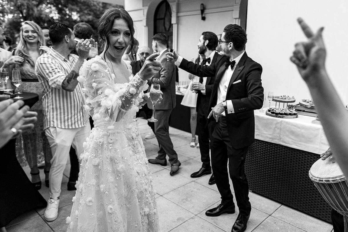 La mari&eacute;e, le verre &agrave; la main, partage un moment de gaiet&eacute; avec les musiciens du 'Groupe Love', les convives en arri&egrave;re-plan partageant cette joie, captur&eacute;e avec authenticit&eacute; par Sebastien CLAVEL Photographe mariage Lyon