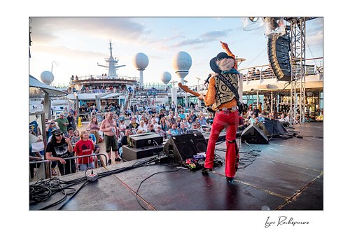 Horizontal color image of Randy Hansen performing from the stage on an outdoor ship deck with a large crowd gathered in front of him