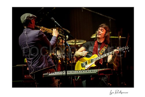 Horizontal color image of Steve Hackett performing with electric guitar alongside a saxophonist on stage