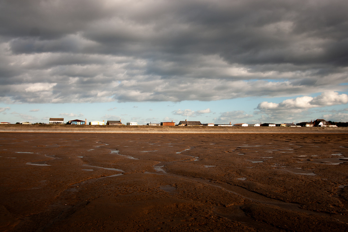 Landscape Photography - Seafront cottages and coastal buildings at Snettisham Beach on the Norfolk coast, viewed across the exposed mudflats at low tide.