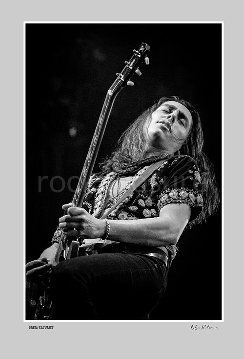 Vertical black and white image of Greta Van Fleet bassist Sam Kiszka performing live on stage