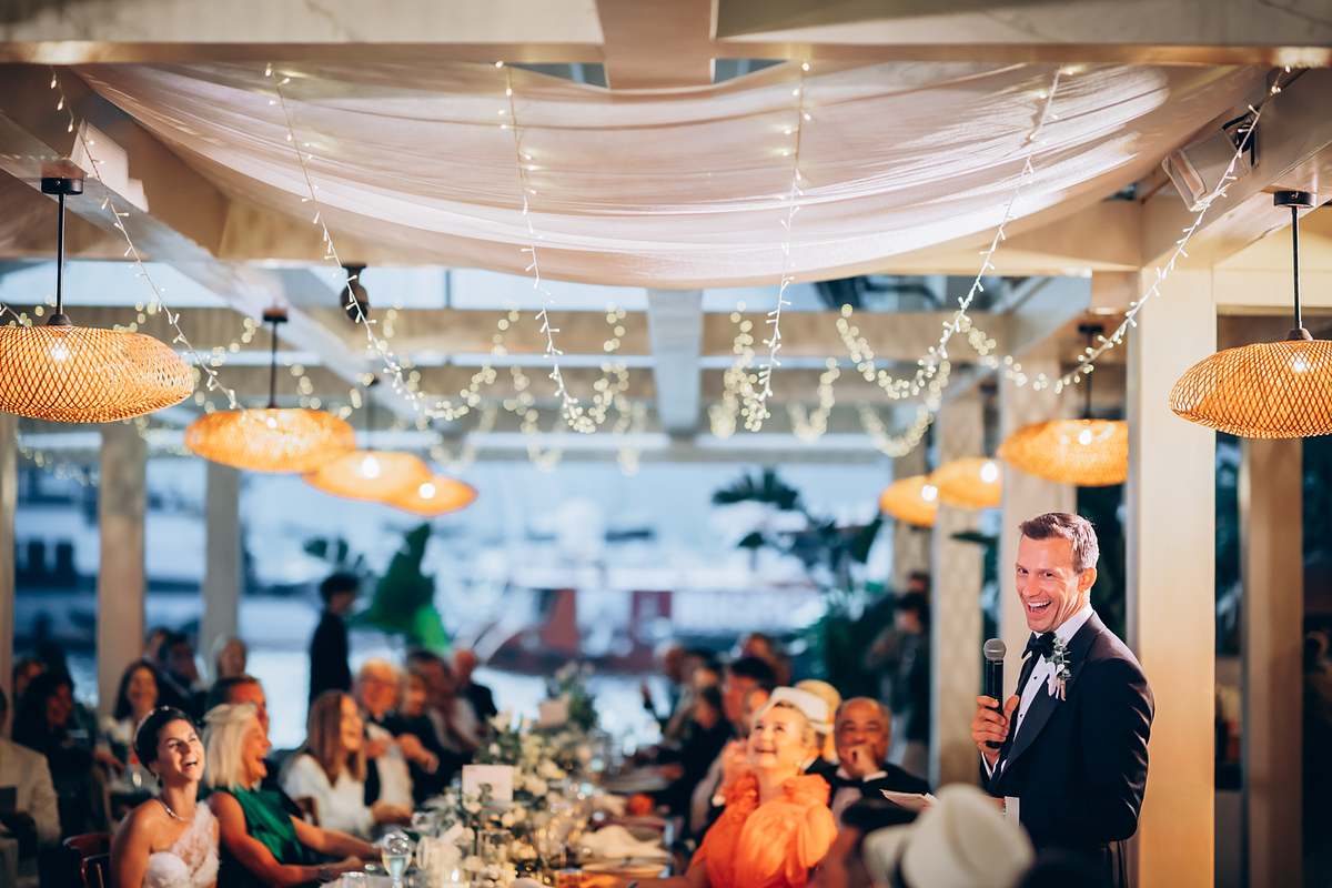 Groom giving a speech as guests laugh during the Göcek wedding dinner