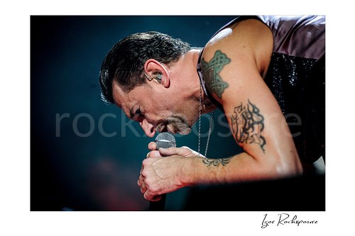 Horizontal color image of Depeche Mode singer Dave Gahan singing into a microphone during a live performance