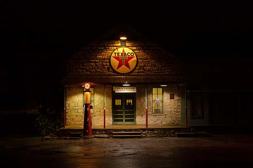 A horizontal fine art night photograph of a historic, illuminated vintage Texaco gas station and antique pump on a quiet Texas back road in Driftwood.