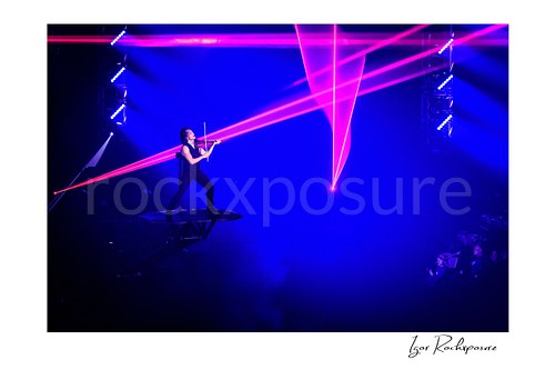 Horizontal color image of Roddy Chong of Trans Siberian Orchestra performing violin on a raised platform beneath pink laser lights