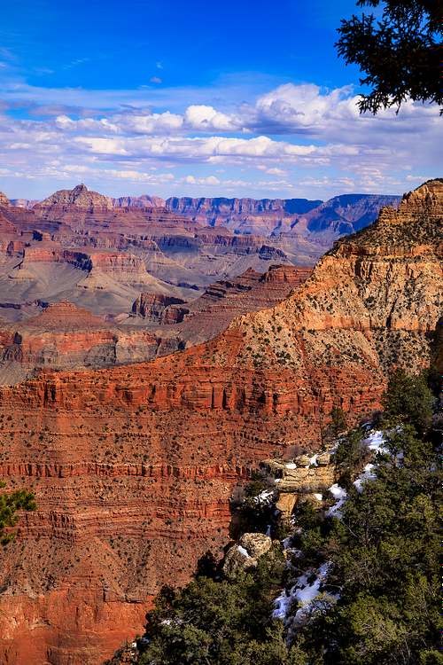 A vertical fine art photograph of the Grand Canyon South Rim in Arizona, highlighting the sheer drop of the canyon walls and towering rock strata under a blue sky.