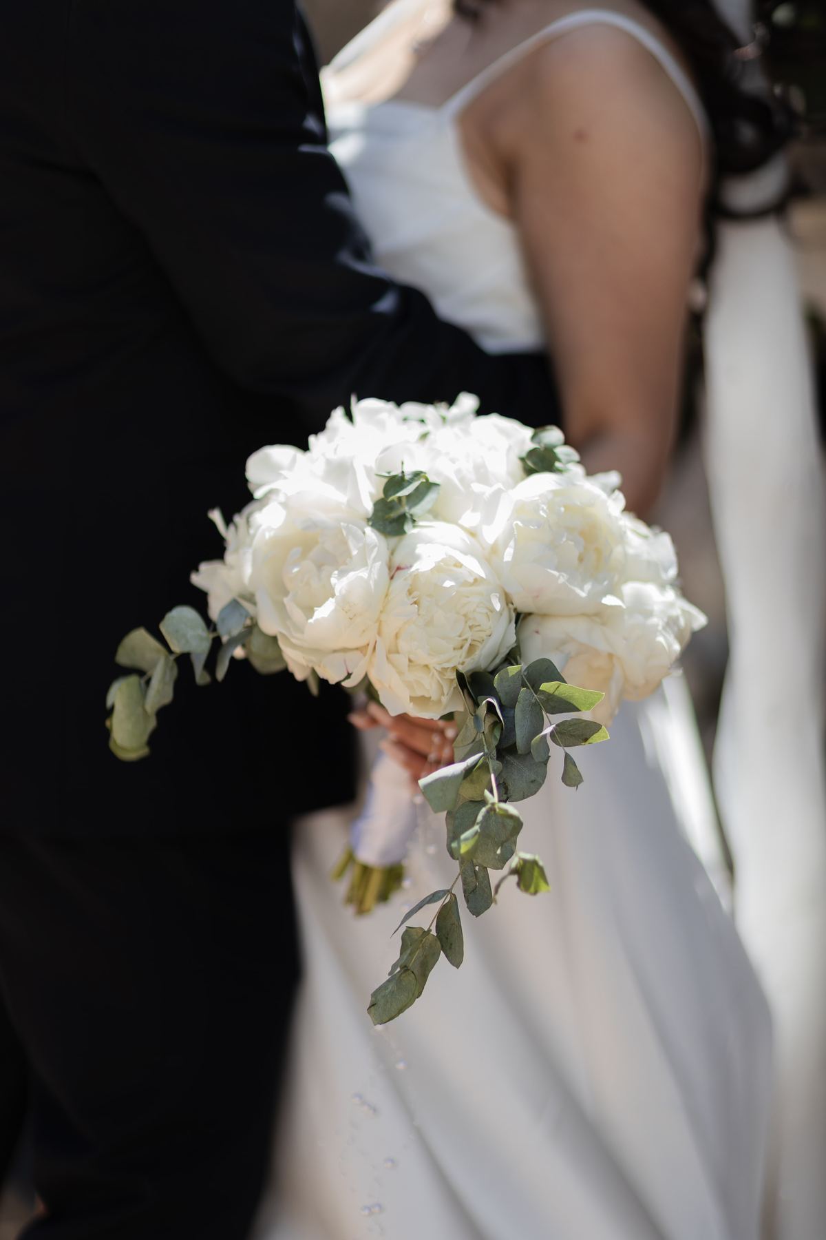 Close-up of white bridal bouquet with bride and groom softly blurred in the background