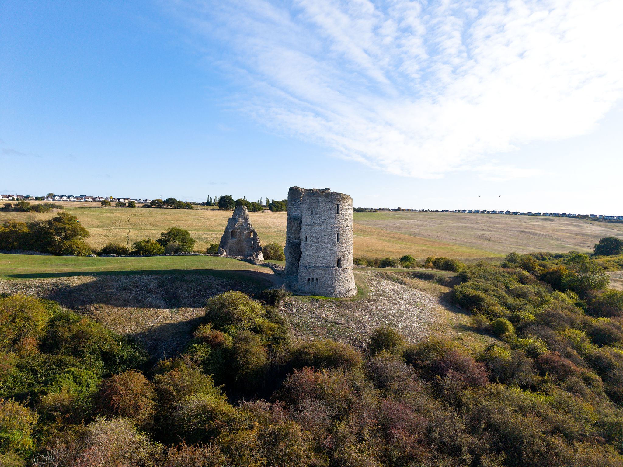 Aerial photograph of a historic stone tower overlooking open fields and woodland in warm evening light.