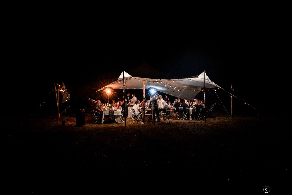Repas sous la tente de r&eacute;ception de mariage brillamment illumin&eacute;e sous un ciel nocturne, captur&eacute;e par S&eacute;bastien Clavel, photographe de mariage &agrave; Lyon et &agrave; N&icirc;mes