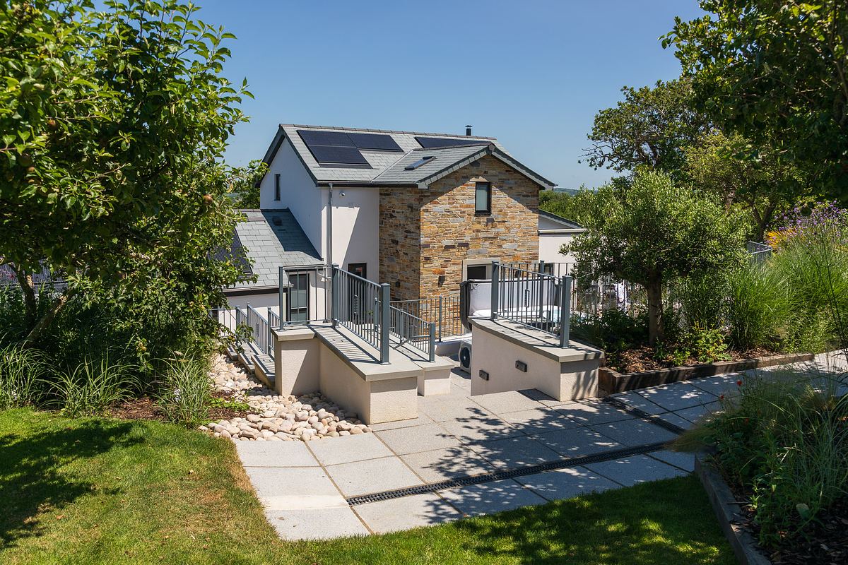 Modern two-story house with stone and white exterior, solar panels on the roof, landscaped yard, and stone path leading to the entrance.
