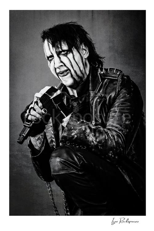 Vertical black and white image of Marilyn Manson holding a microphone in a tight theatrical portrait