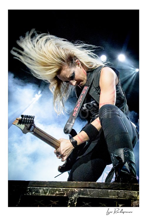 Vertical color image of Nita Strauss performing live on stage with an electric guitar and dramatic flying hair