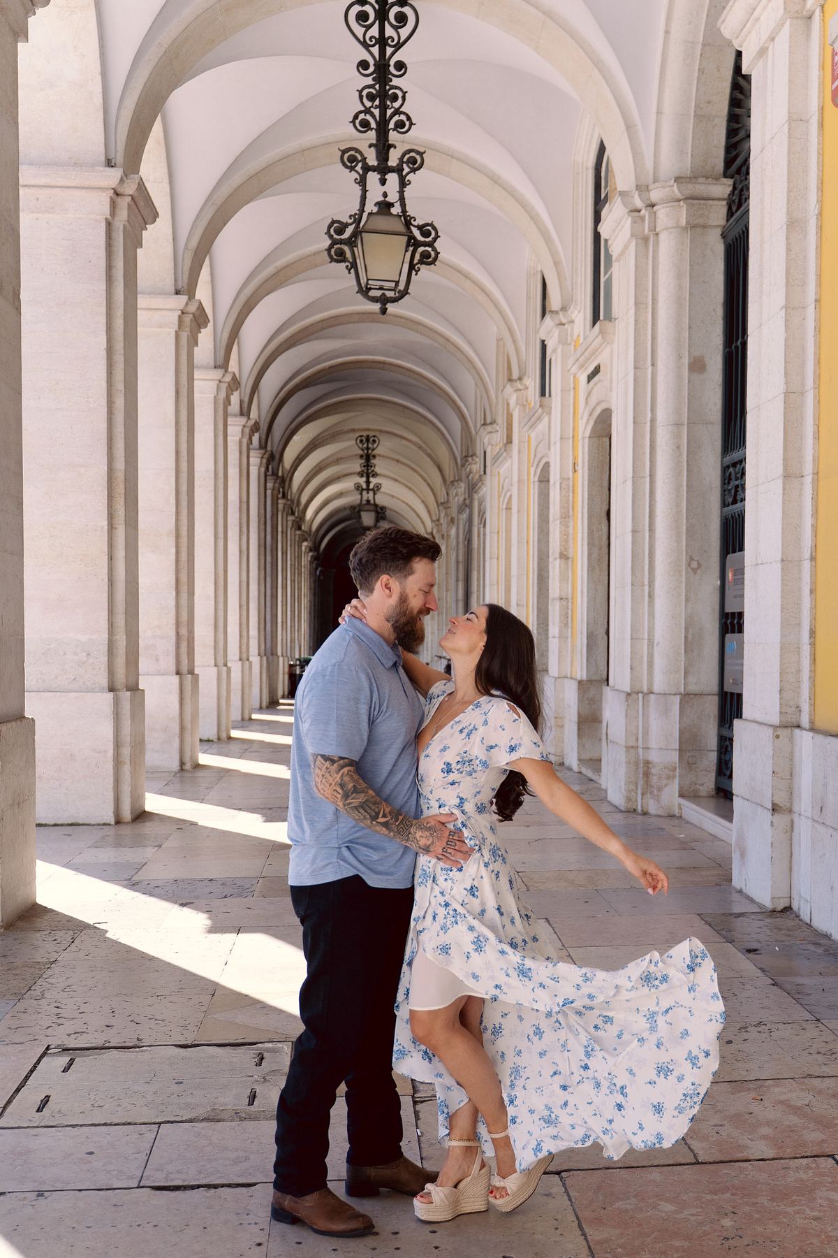 Engaged couple posing beneath the historic arcades of Pra&ccedil;a do Com&eacute;rcio