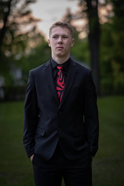 Photo of Prince Albert Grad in a suit standing in PACI's school grounds at sunset.