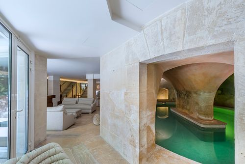 Vue depuis l'intérieur vers la piscine sous les voûtes en pierre à Saint-Germain-des-Prés, avec mur en pierre et salon en arrière-plan. Photographie d'architecture intérieure par Nicolas Karadimos.