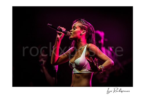 Horizontal color image of Rihanna singing into a microphone in side profile under vivid magenta stage lighting