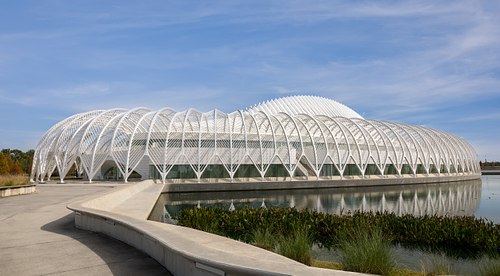 A wide-angle hero shot of the Florida Polytechnic University IST building by Santiago Calatrava, showcasing the iconic white louvered roof and its reflection in the surrounding water.