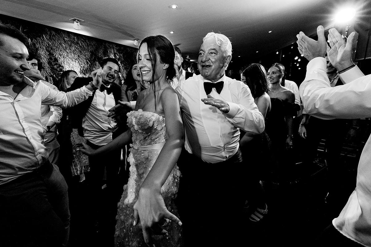 Un instant festif en noir et blanc o&ugrave; la mari&eacute;e danse entour&eacute;e de convives enthousiastes, du p&egrave;re du mari&eacute; au sourire contagieux &agrave; ses c&ocirc;t&eacute;s, captur&eacute; au Pavillon du Casino Lyon vert par Sebastien CLAVEL Photographe mariage Lyon