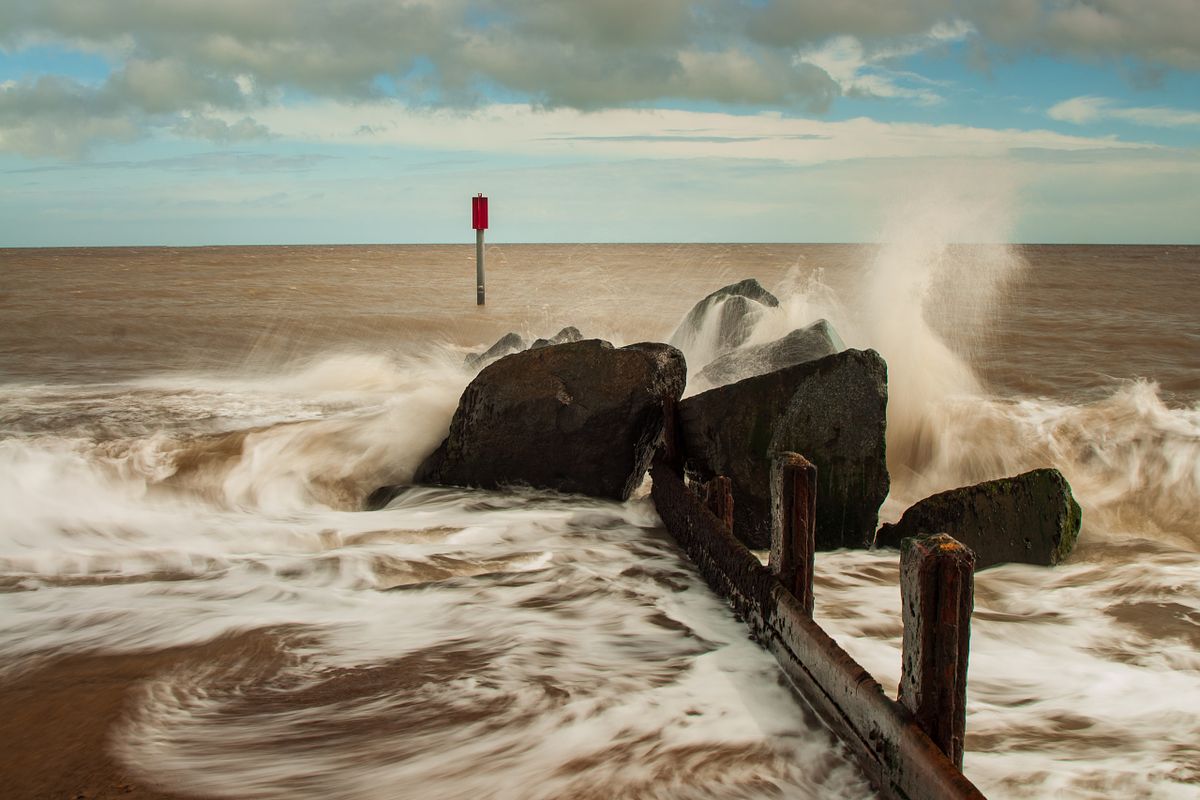 Waves crashing over wooden sea defences on the Norfolk coast.