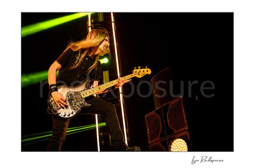 Horizontal color image of James LoMenzo of Megadeth playing bass on stage with long hair and green concert lights
