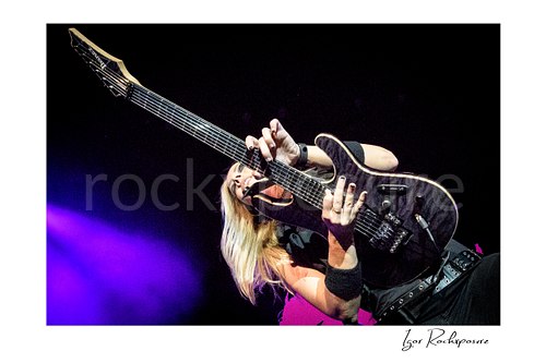 Horizontal color image of Nita Strauss performing live on stage with an electric guitar