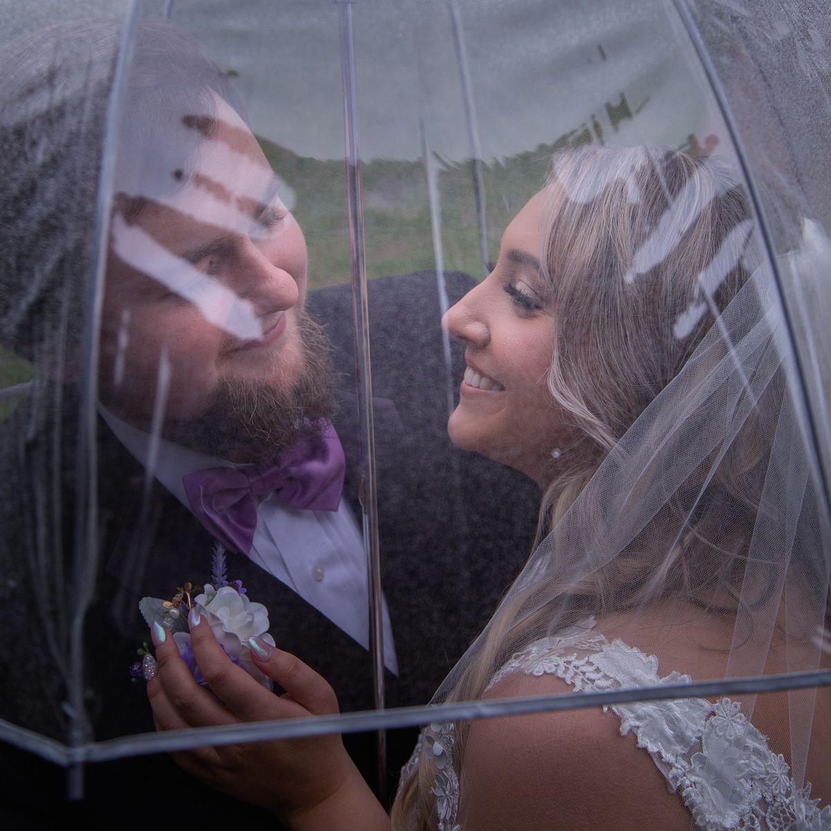 bride and groom under an umbrella embracing the rain and hugging closely