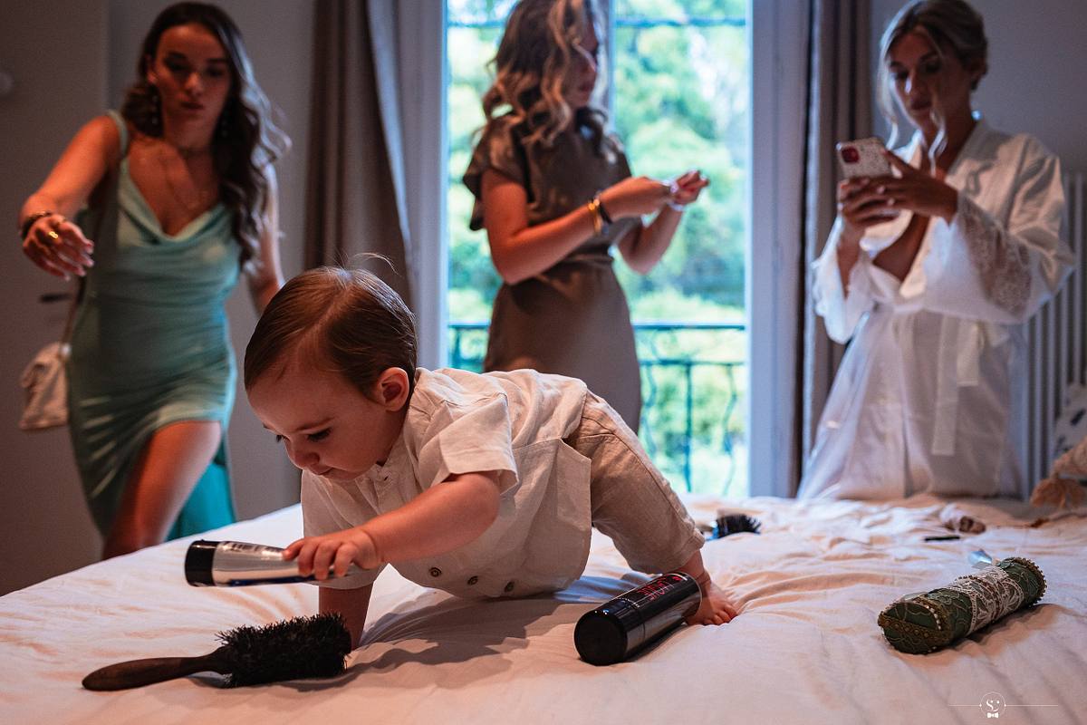 Moment familial avec la mari&eacute;e en peignoir regardant son enfant, entour&eacute;e de proches dans une chambre pr&eacute;paratoire lumineuse, captur&eacute; par S&eacute;bastien Clavel &agrave; N&icirc;mes