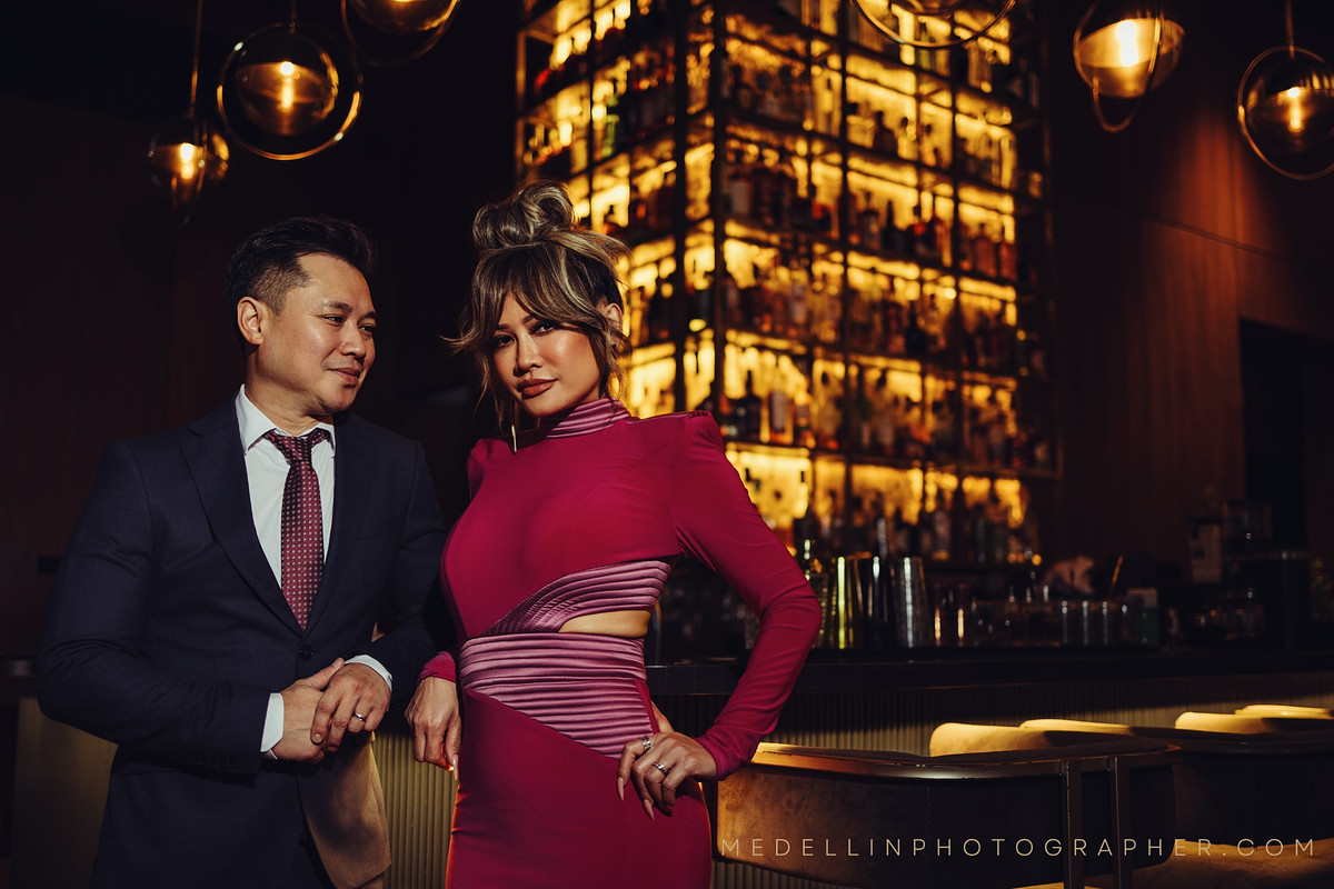 Couple in formal wear posing inside a warmly lit Medellin cocktail bar