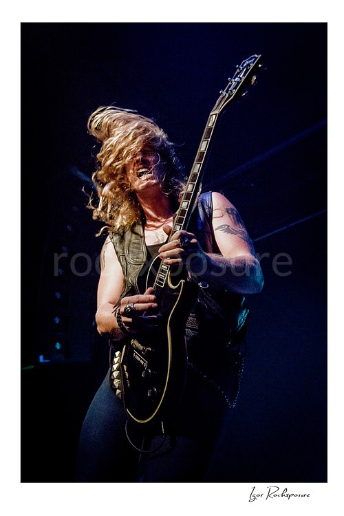 Vertical color image of Jared James Nichols playing guitar onstage with flying hair under blue concert light