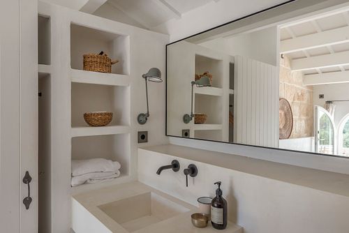 Salle de bains avec vasque en pierre, grand miroir et étagères intégrées dans la finca Son Fonoll à Minorque. Photographie par Nicolas Karadimos.