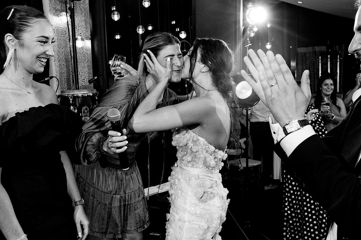 La mari&eacute;e &eacute;change un baiser tendre avec un invit&eacute;, sous les applaudissements joyeux d'amis souriants, capture de joie spontan&eacute;e au Pavillon du Casino Lyon vert par Sebastien CLAVEL Photographe mariage Lyon
