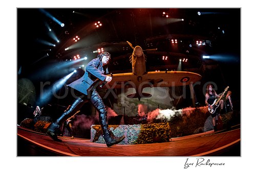 Bruce Dickinson and Steve Harris of Iron Maiden performing live on stage beneath a large airplane stage prop with dramatic lighting and smoke effects.