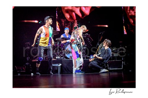 Anthony Kiedis stands beside Chad Smith’s drum riser as Flea faces a kneeling Josh Klinghoffer, all four Red Hot Chili Peppers members on stage.
