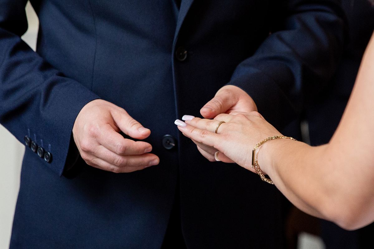 Close-up of groom holding bride's hand and wedding ring during the ceremony