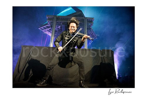 Horizontal color image of Roddy Chong of Trans Siberian Orchestra performing violin on stage with flying hair and blue concert lighting
