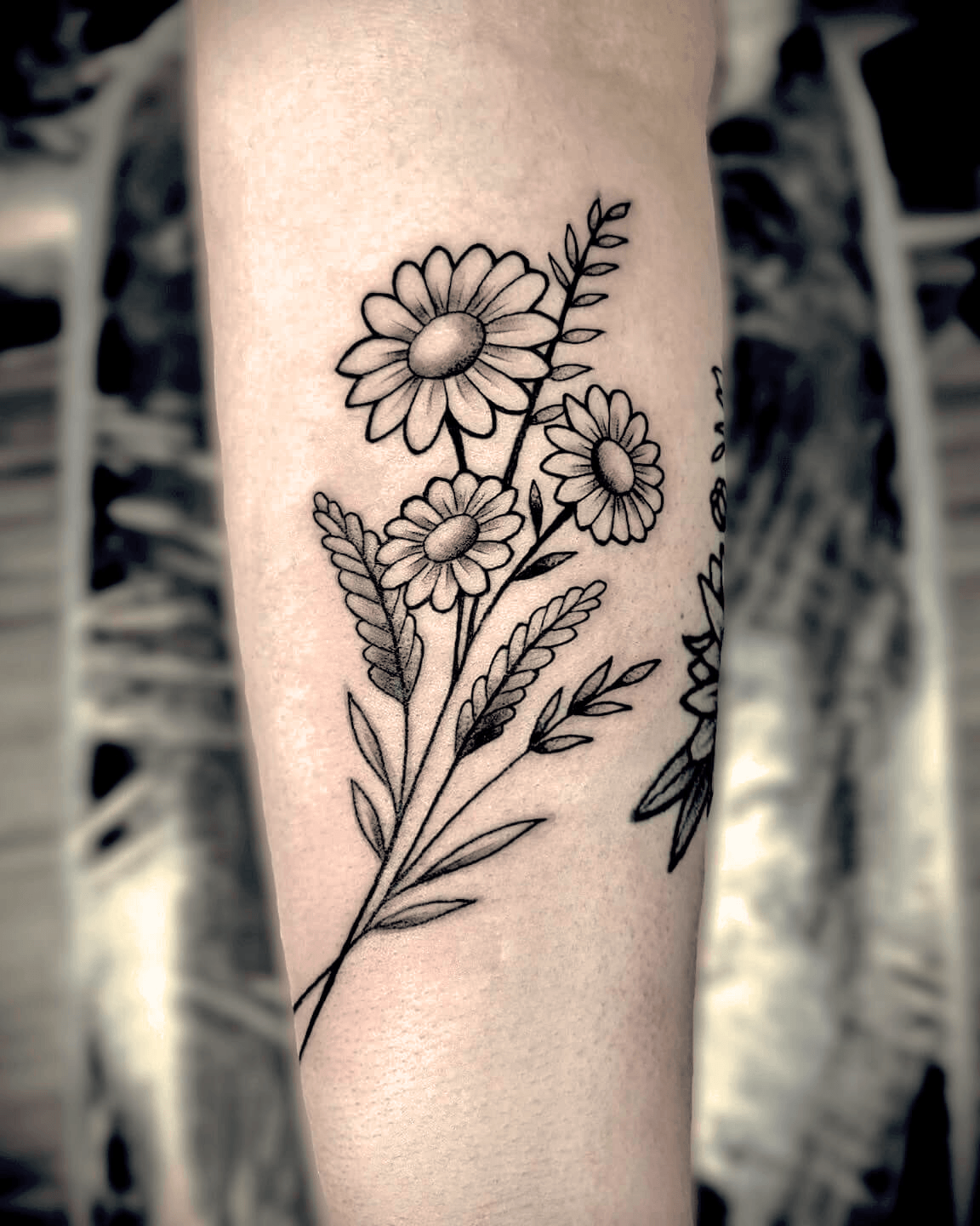 Fine line wrist tattoo featuring a daisy and lavender sprigs in delicate black ink linework, small botanical design created in Stoke-on-Trent by Alika Tattoo Art.