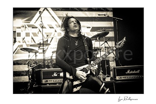 Horizontal black and white image of Michael Sweet of Stryper performing live with a striped electric guitar on stage