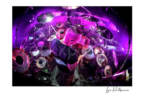 Horizontal color image of Korn drummer Ray Luzier seen from above at the drums under vivid purple stage lighting